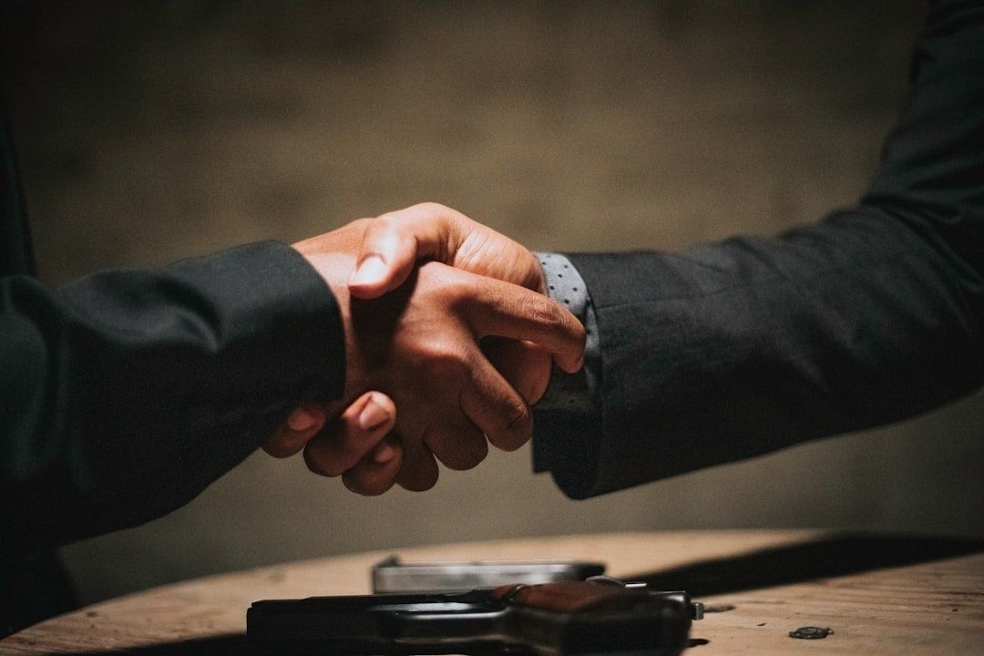 Deux personnes se serrent la main au-dessus d’un bureau, avec une mallette